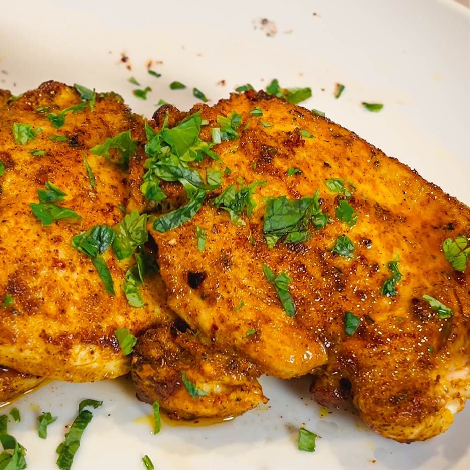 Two chicken breasts beautifully seared with Mediterranean spice blend "Grill Thrill". Topped with chopped parsley garnish.