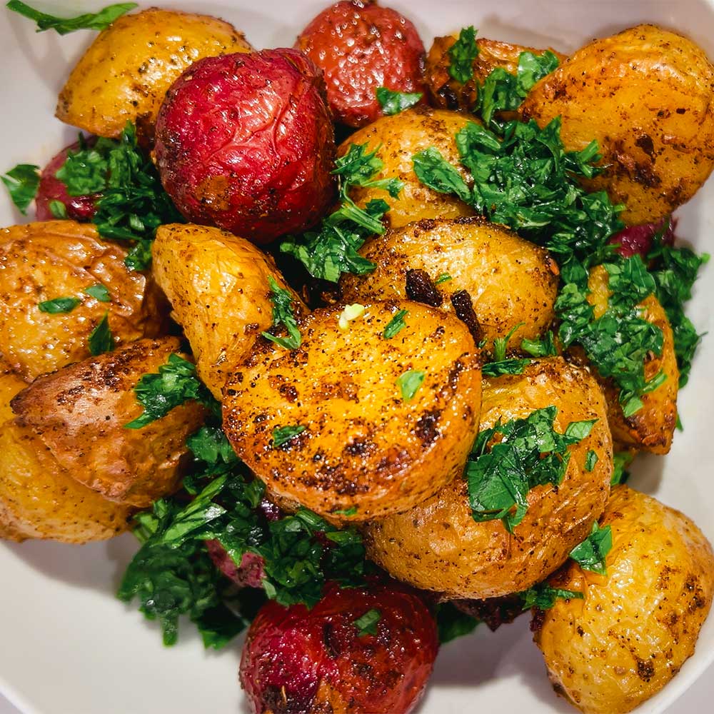 Bowl with beautiful roasted potatoes made with Mediterranean spice blend "Potayto-Potahto". Garnished with chopped parsley.
